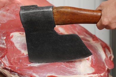 Photo of Butcher chopping fresh raw meat with axe in shop, closeup