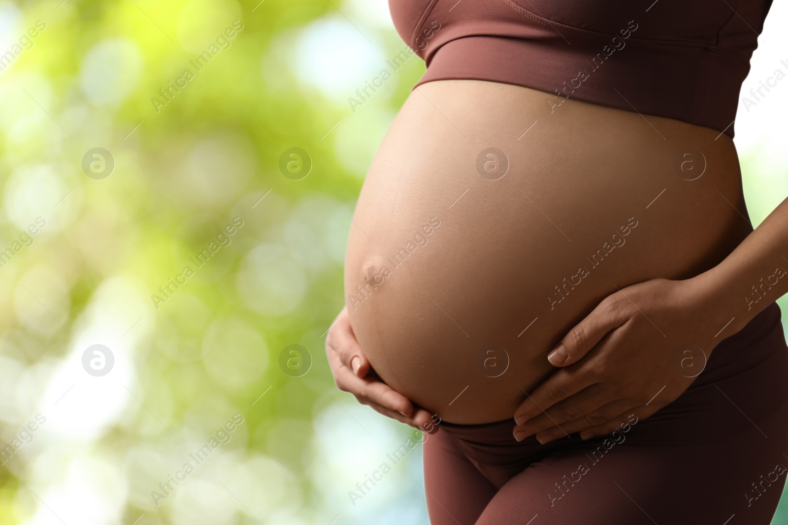 Image of Young pregnant woman touching her belly outdoors, closeup. Space for text