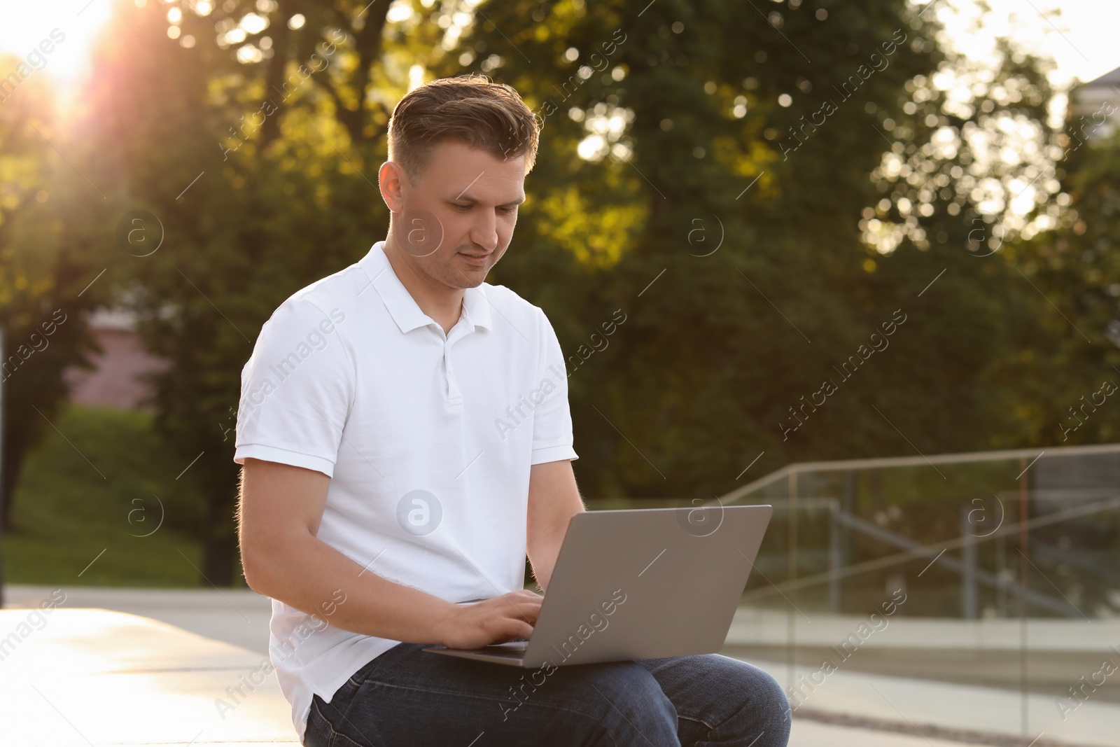 Photo of Handsome man using laptop on bench outdoors