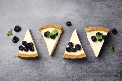 Photo of Pieces of delicious cheesecake with blackberries on grey background, flat lay