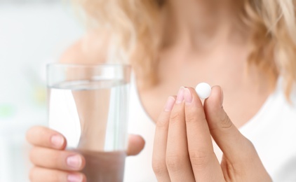 Young woman with pill and glass of water indoors