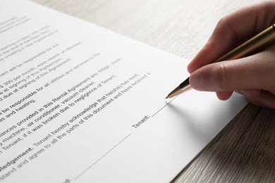 Woman signing document with pen at wooden table, closeup