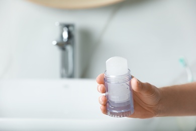 Photo of Woman holding crystal alum deodorant in bathroom, closeup. Space for text