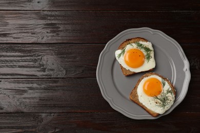 Photo of Plate with tasty fried eggs, slices of bread and dill on dark wooden table, top view. Space for text