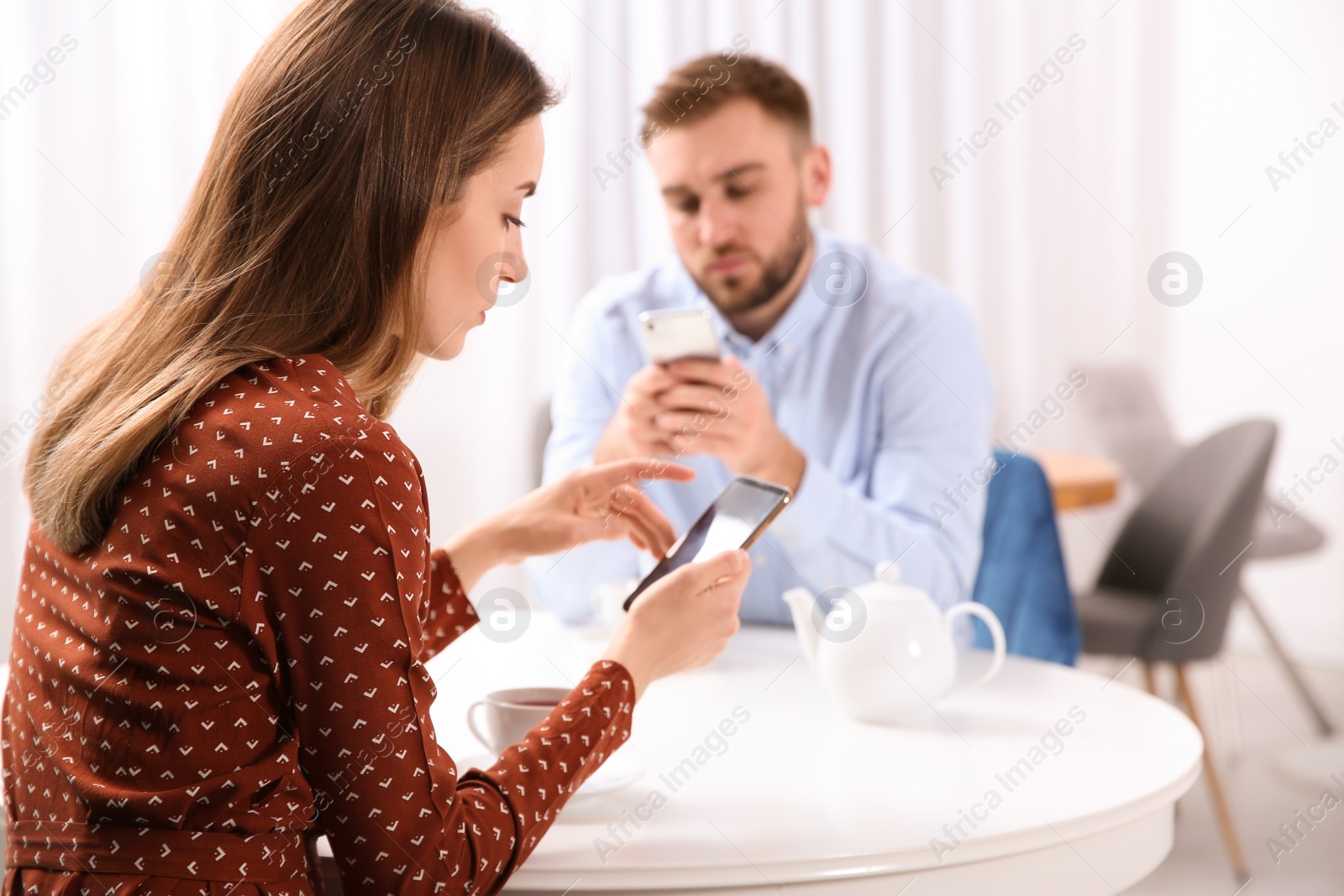 Photo of Couple addicted to smartphones ignoring each other in cafe. Relationship problems