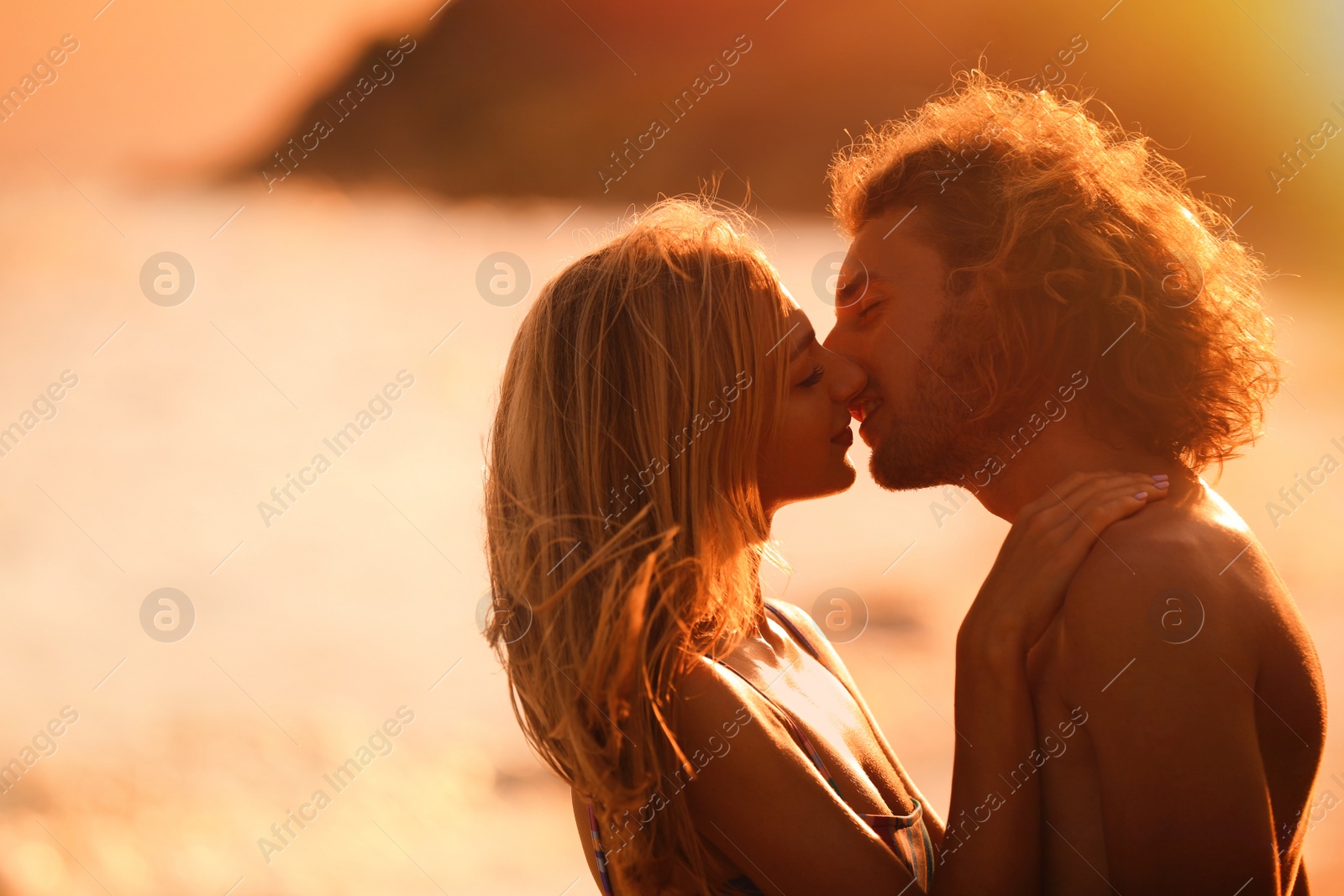 Photo of Young woman in bikini kissing her boyfriend on beach at sunset. Lovely couple