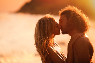 Young woman in bikini kissing her boyfriend on beach at sunset. Lovely couple