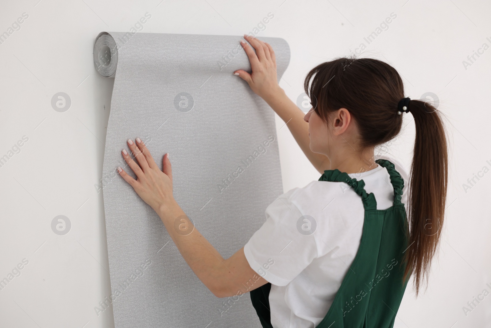 Photo of Woman hanging stylish gray wallpaper in room