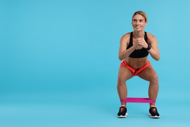 Woman exercising with elastic resistance band on light blue background. Space for text