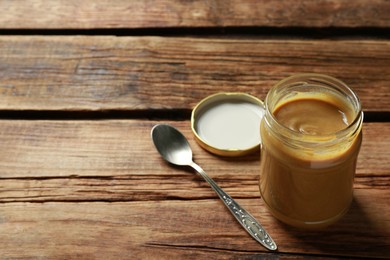 Photo of Spicy mustard in glass jar and spoon on wooden table. Space for text