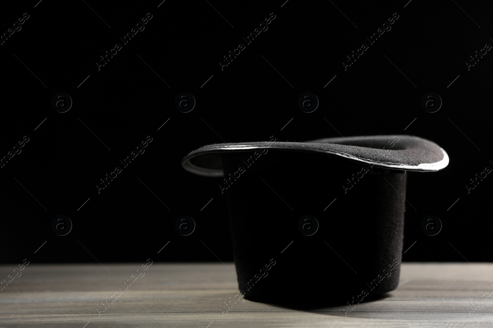 Photo of Magician's hat on white wooden table against black background, space for text