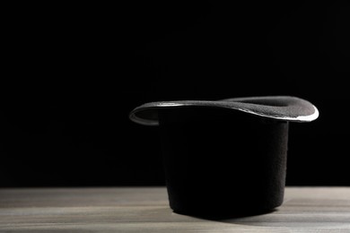 Photo of Magician's hat on white wooden table against black background, space for text