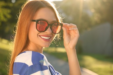 Beautiful smiling woman wearing sunglasses in park, space for text