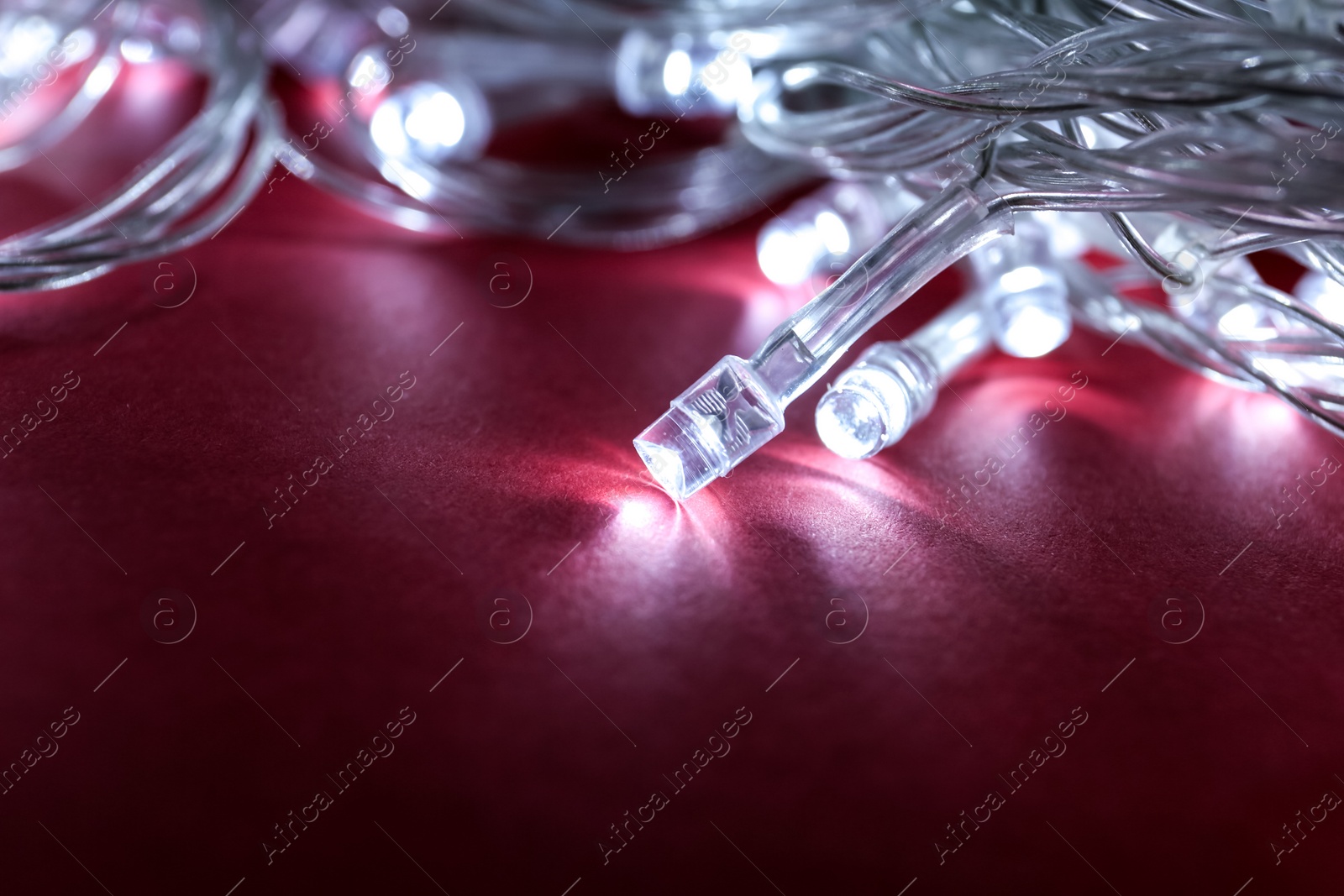 Photo of Glowing Christmas lights on burgundy background, closeup