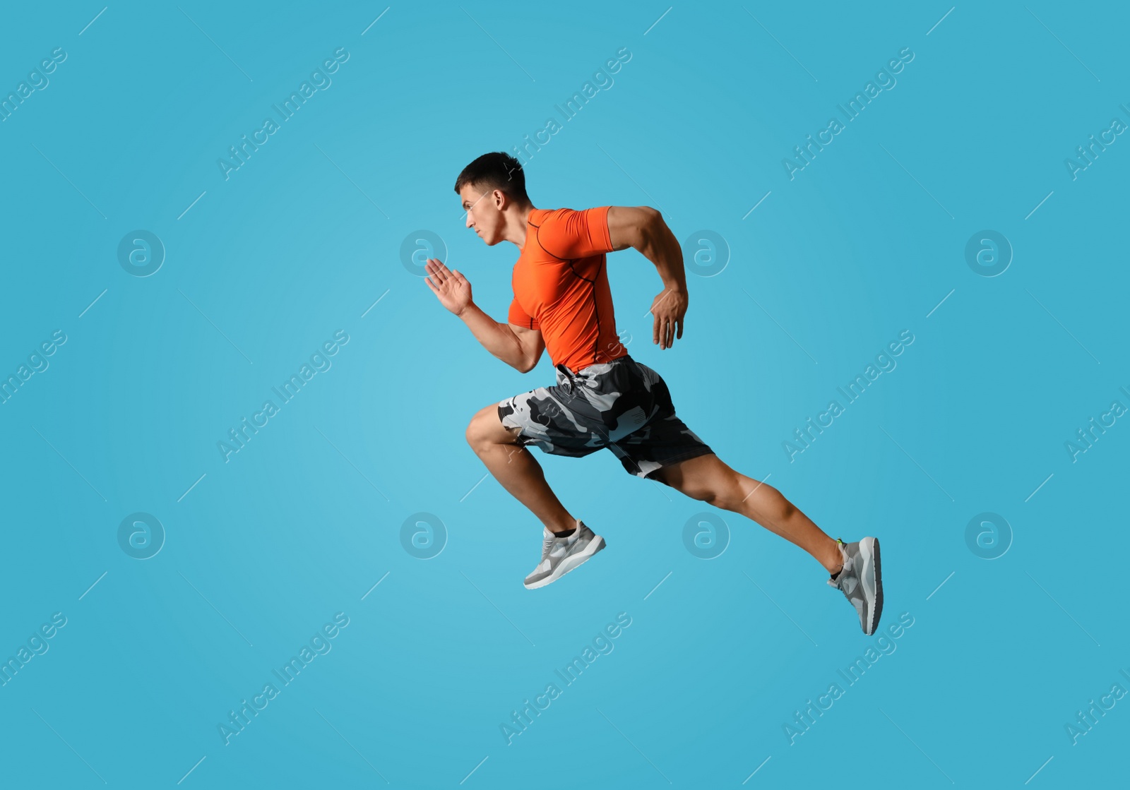 Photo of Athletic young man running on light blue background, side view