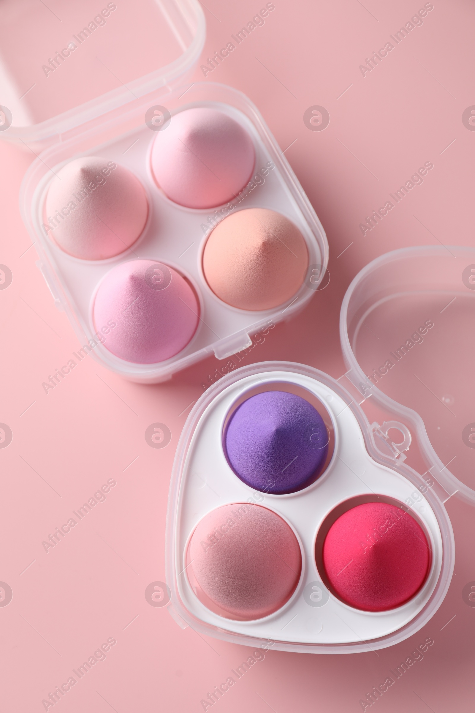 Photo of Makeup sponges in plastic containers on pink background, top view