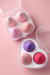 Photo of Makeup sponges in plastic containers on pink background, top view