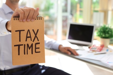 Photo of Man holding notebook with words TAX TIME indoors