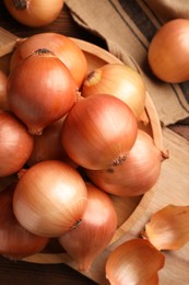 Many ripe onions on wooden table, flat lay