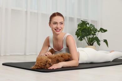 Happy young woman practicing yoga on mat with her cute dog indoors