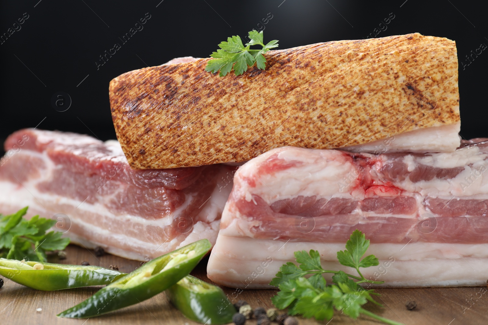 Photo of Pieces of raw pork belly, chili pepper, peppercorns, oil and parsley on wooden board, closeup