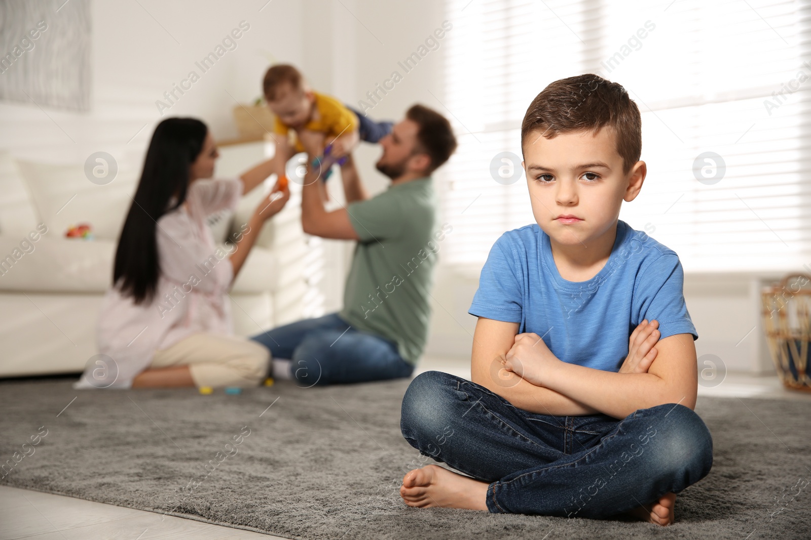 Photo of Unhappy little boy feeling jealous while parents spending time with his baby brother at home