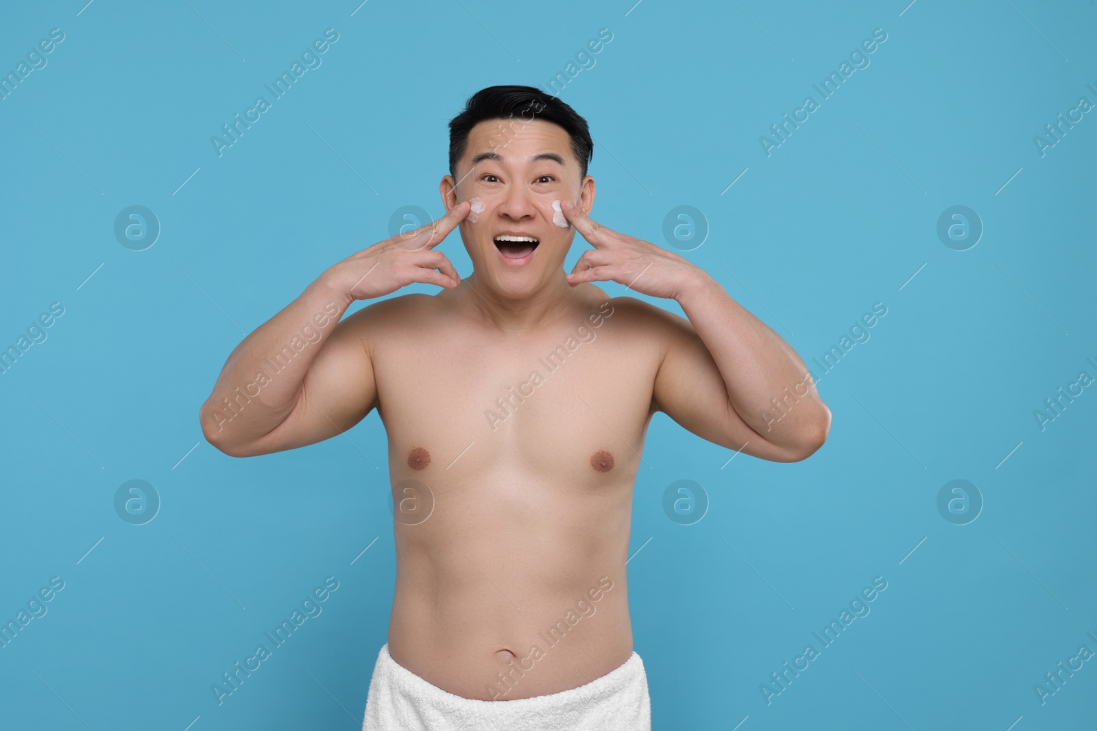 Photo of Emotional man applying cream onto his face on light blue background