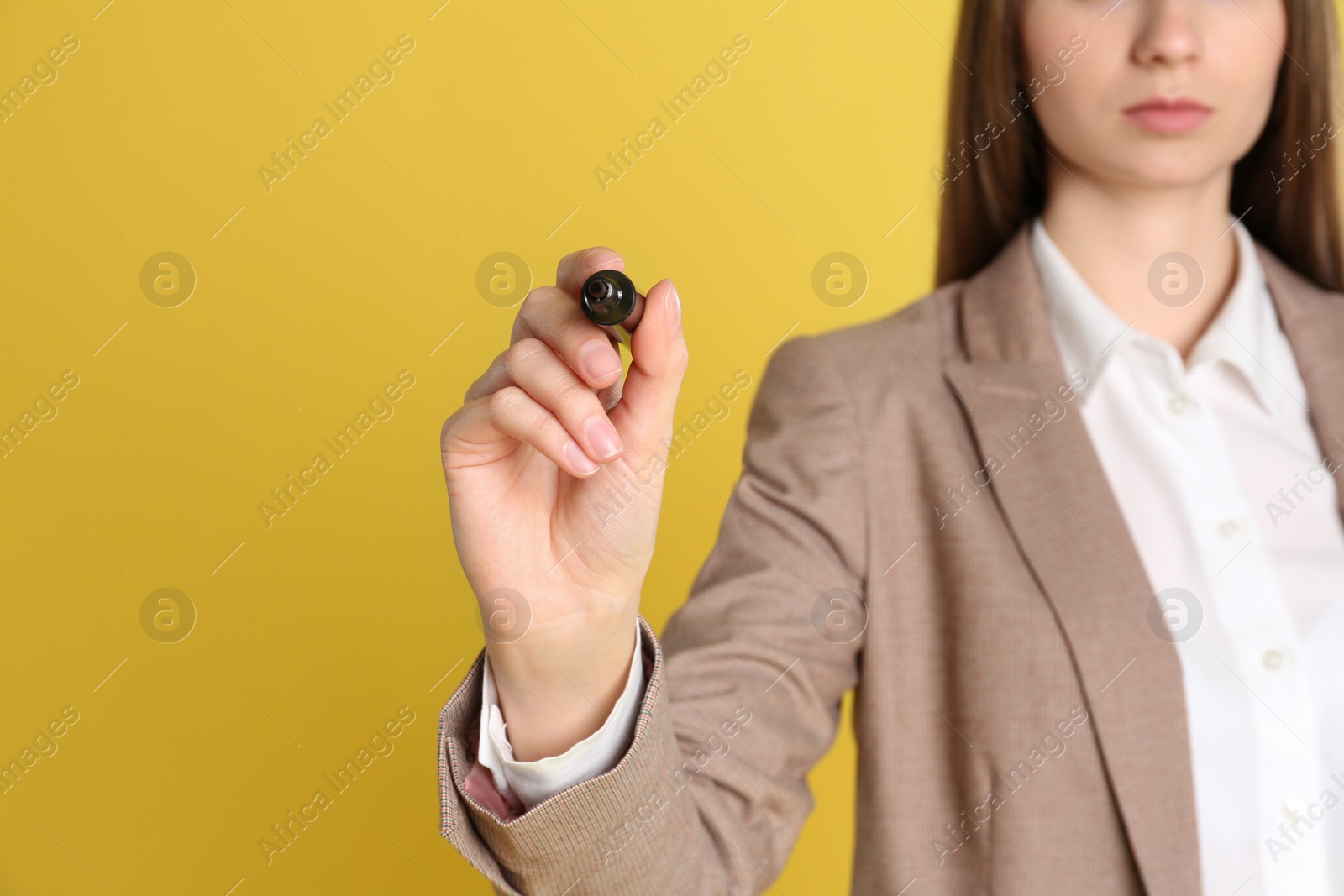 Photo of Young woman with marker against yellow background, focus on hand