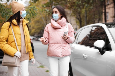 Photo of Young women in medical face masks walking outdoors. Personal protection during COVID-19 pandemic