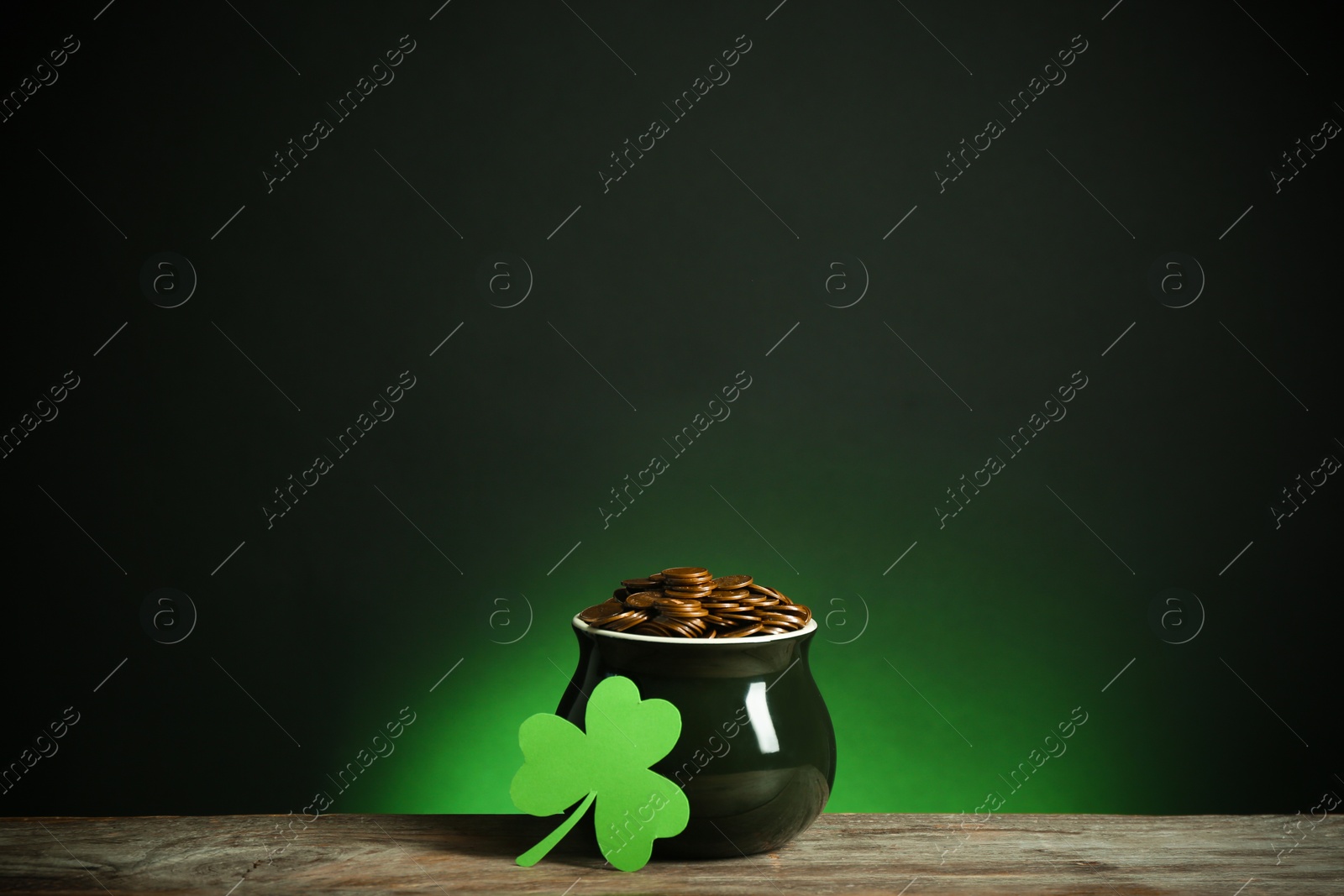 Photo of Pot with gold coins and clover on wooden table against dark background. St. Patrick's Day