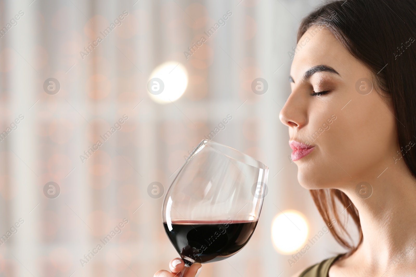 Photo of Beautiful young woman with glass of luxury red wine indoors, closeup view. Space for text