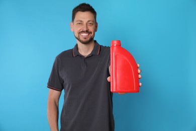 Man showing motor oil against light blue background, focus on container