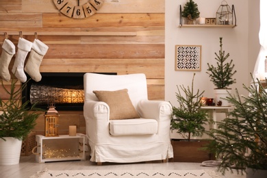 Potted fir trees and Christmas decorations in room with fireplace. Stylish interior design