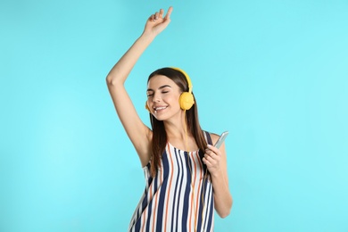 Beautiful young woman listening to music with headphones on color background