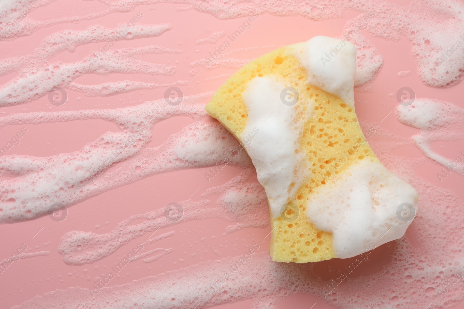 Photo of Yellow sponge with foam on pink background, top view