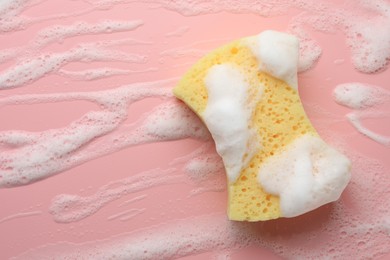 Yellow sponge with foam on pink background, top view