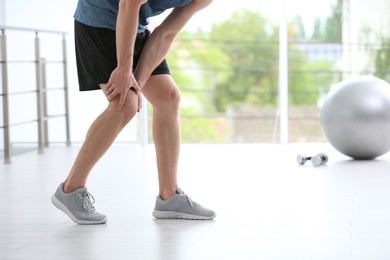 Man in sportswear suffering from knee pain at gym, closeup