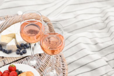 Photo of Glasses of delicious rose wine, food and basket on white picnic blanket, space for text