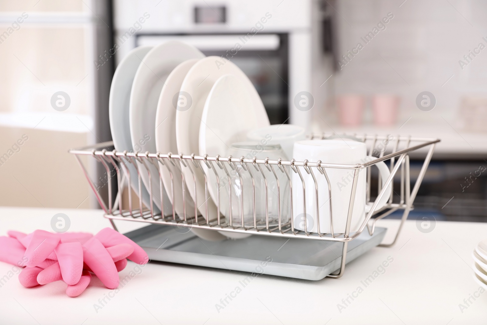 Photo of Dish drainer with clean dinnerware on table in kitchen