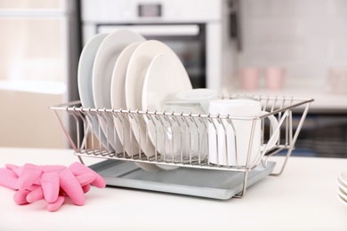 Dish drainer with clean dinnerware on table in kitchen