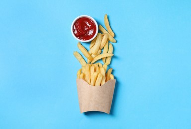 Paper cup with French fries and ketchup on light blue table, flat lay