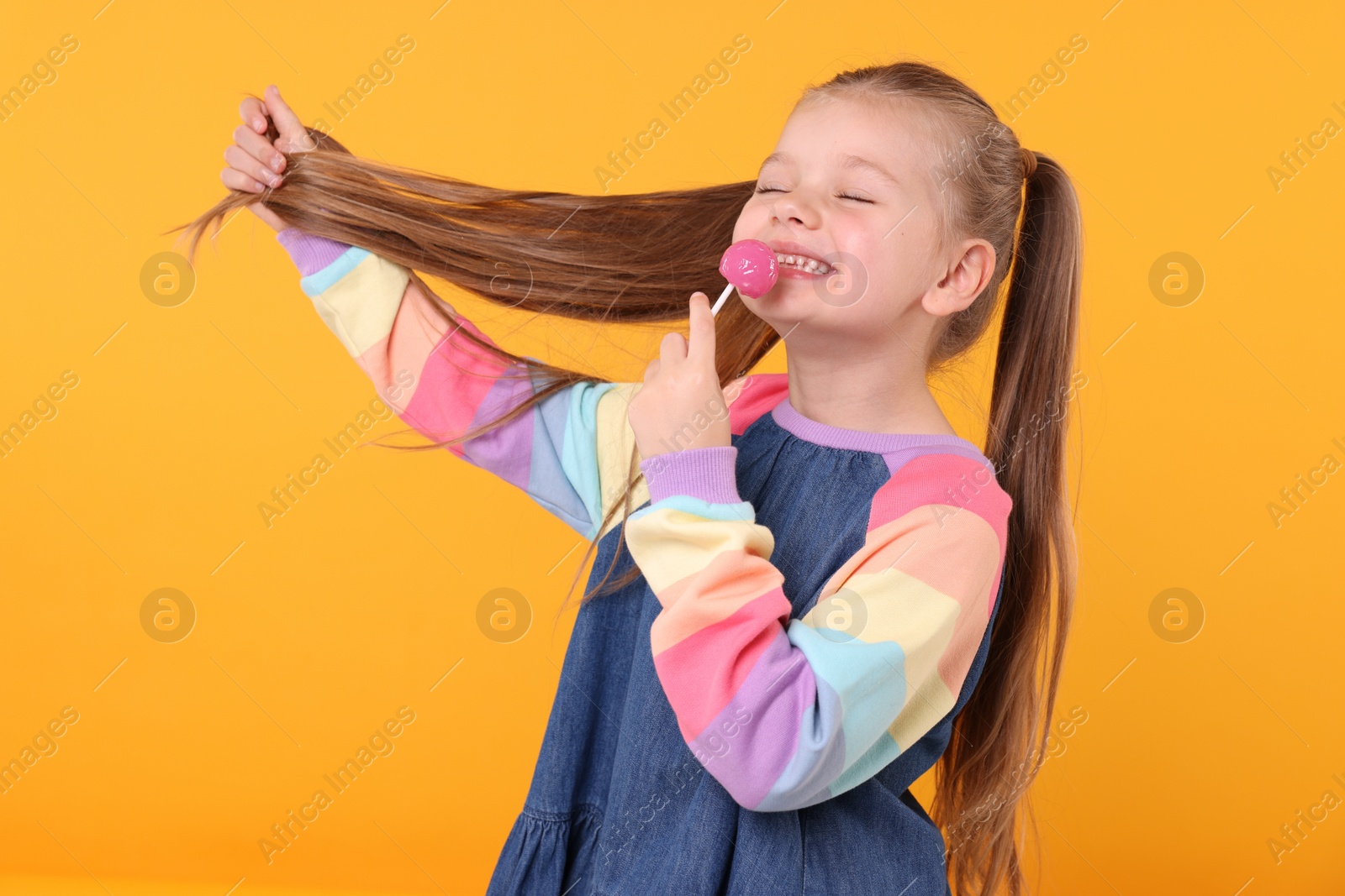 Photo of Happy little girl with lollipop on orange background