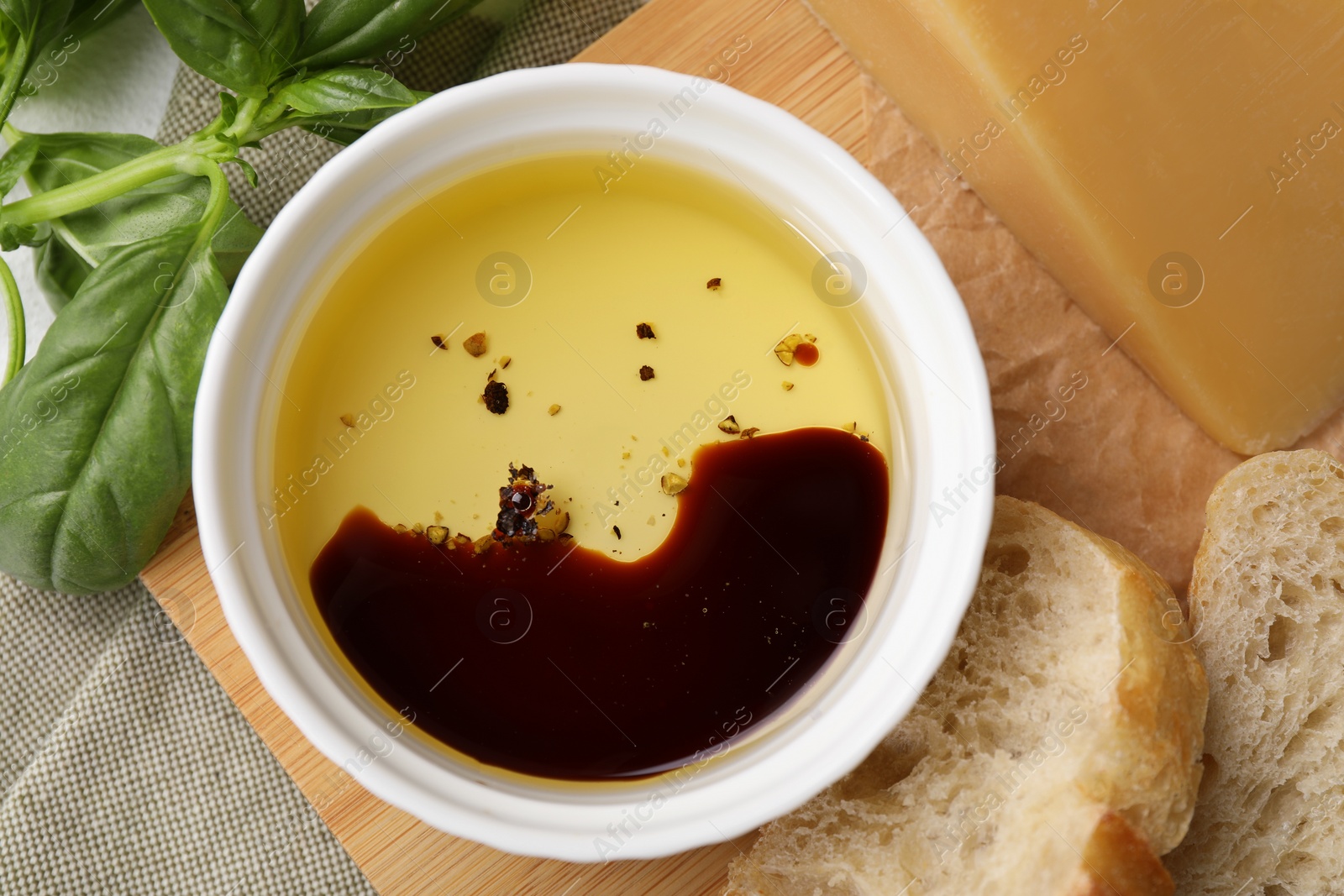 Photo of Bowl of organic balsamic vinegar with oil, basil, bread and cheese on table, flat lay