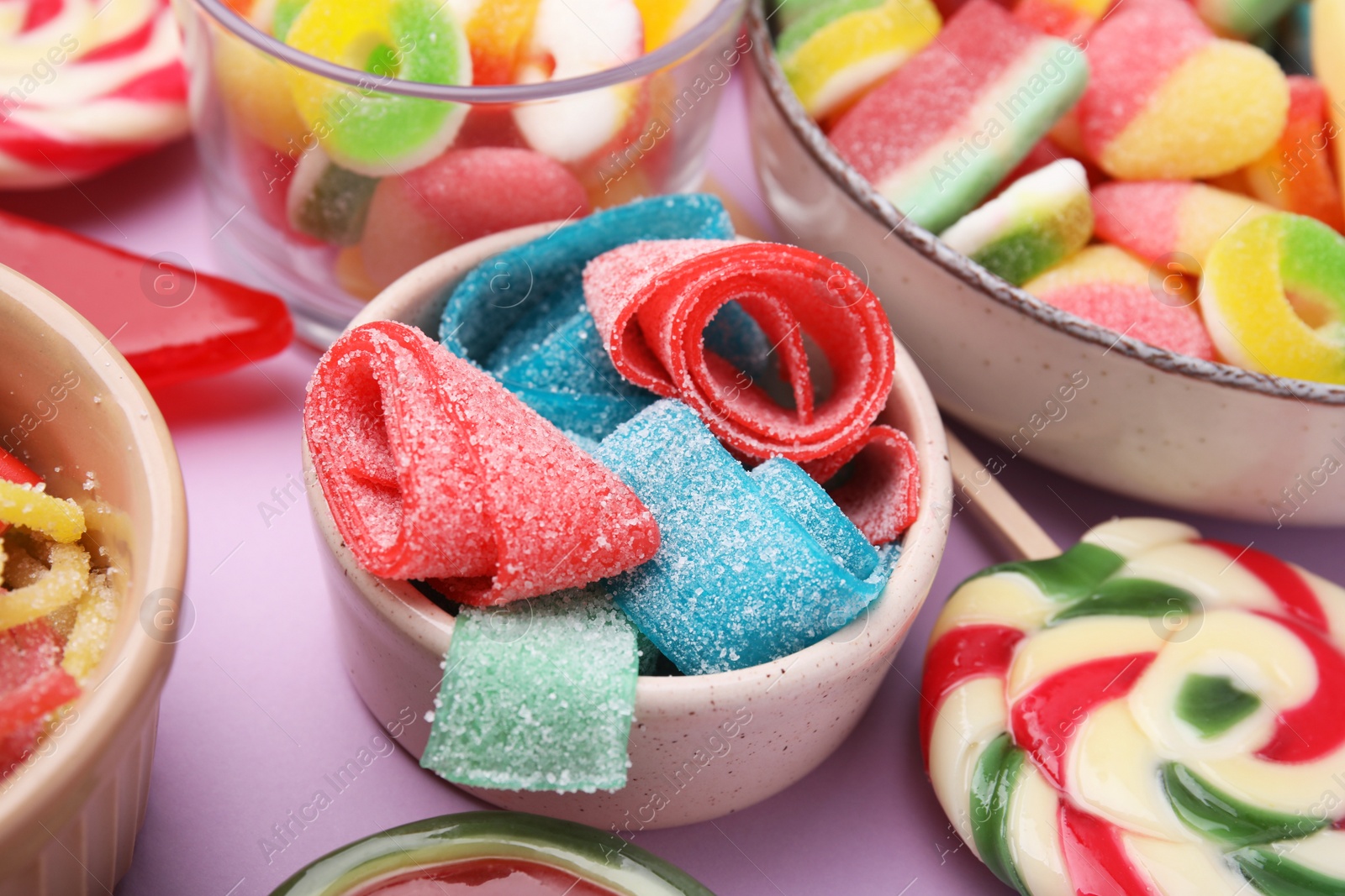 Photo of Many different jelly candies on lilac background, closeup