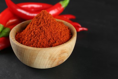 Photo of Paprika powder and fresh chili peppers on black table, closeup. Space for text