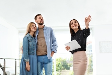Photo of Female real estate agent showing new house to couple, indoors