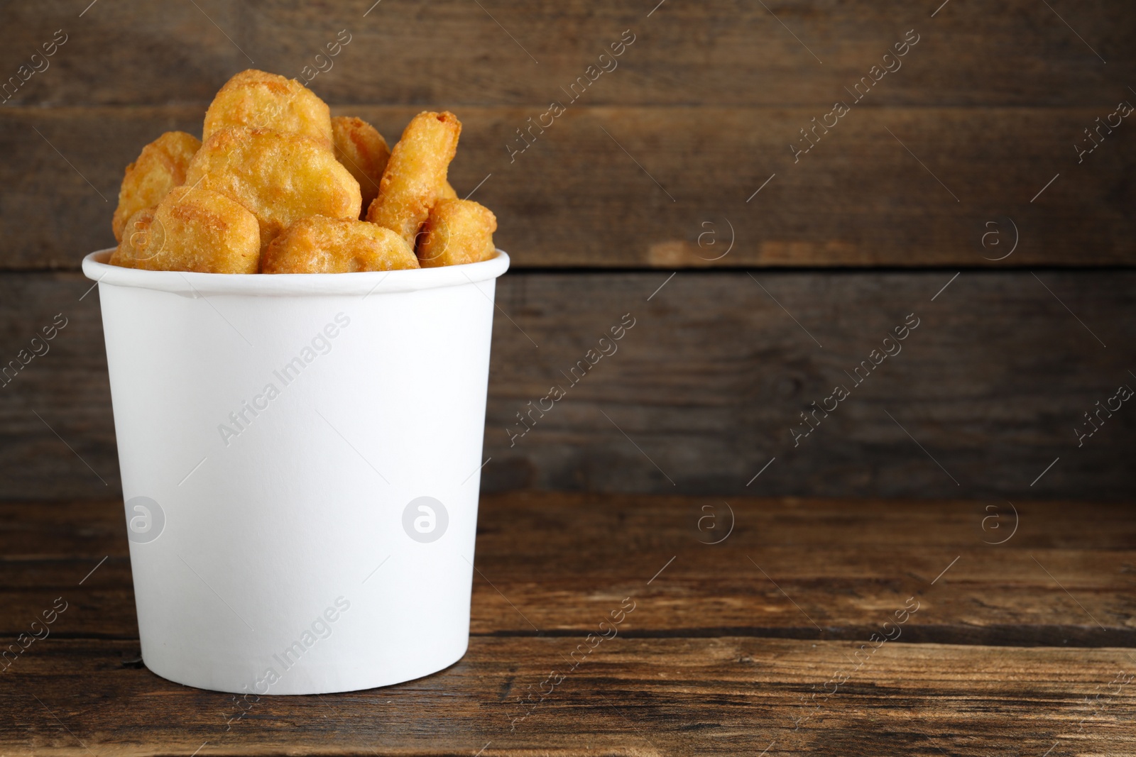 Photo of Bucket with tasty chicken nuggets on wooden table. Space for text