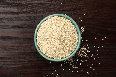Photo of Dry quinoa seeds in bowl on wooden table, top view