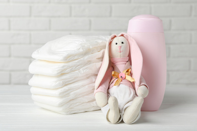 Photo of Baby diapers, toy bunny and bottle on wooden table against white brick wall