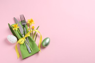 Photo of Cutlery set, Easter eggs and narcissuses on pale pink background, flat lay with space for text. Festive table setting